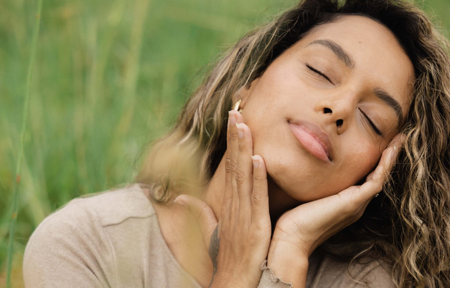 Woman closing her eyes with her hands resting on her face while kneeling in the grass