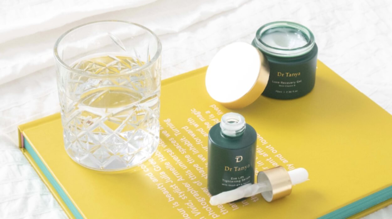 Two green skincare products and a glass of water on a yellow book